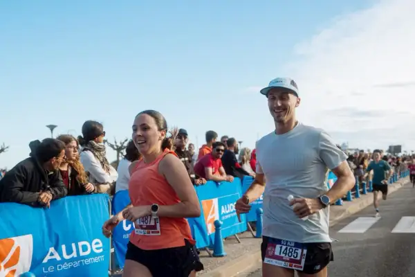 Un couple court joyeusement lors d'un marathon, le soleil brille sur la côte indigo.