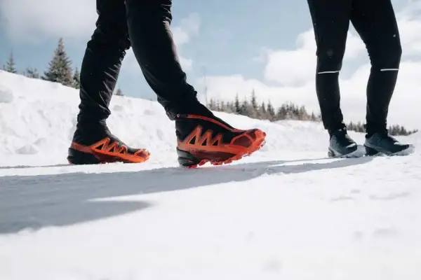 Deux personnes en chaussures de trail, l'une avec des chaussures orange vif, parcourent un sentier enneigé du Haut Giffre.