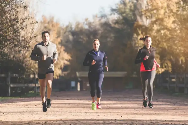 Trois coureurs s'entraînent pour un marathon, profitant d'une journée ensoleillée dans un parc.