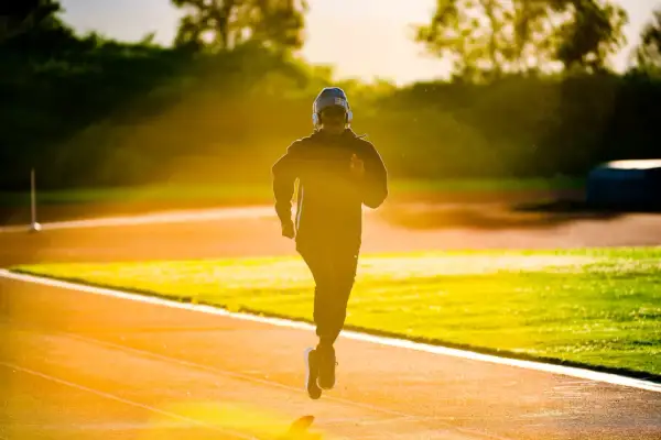 Un jeune homme court sur une piste d'athlétisme à Lyon, baigné par la lumière dorée du soleil couchant.