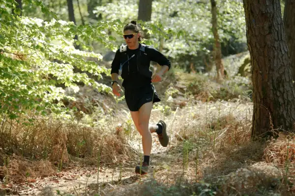 Un coureur s'entraîne dans une forêt ensoleillée, prêt à courir avant une course.