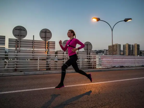 Une femme en tenue de sport rose et noire court sur une route au crépuscule, profitant d'une course de nuit sous les lampadaires.