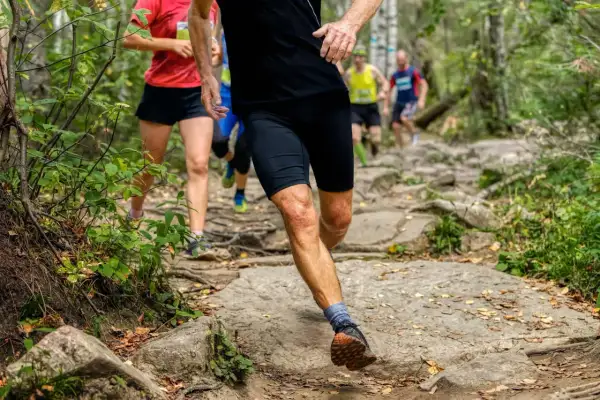 Des coureurs s'élancent sur un sentier rocailleux en pleine forêt. Leurs jambes en pleine action montrent l'effort du running et du jogging.