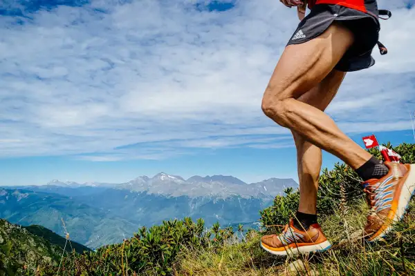 Un coureur en plein entrainement trail, jambes musclées, sur un sentier de montagne avec un panorama spectaculaire.