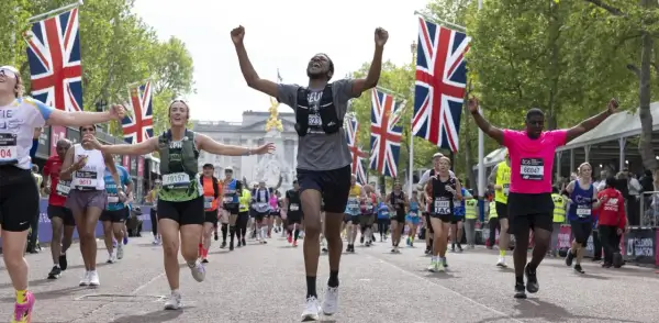 Des coureurs célèbrent leur arrivée au plus grand marathon du monde, drapeaux britanniques en arrière-plan.