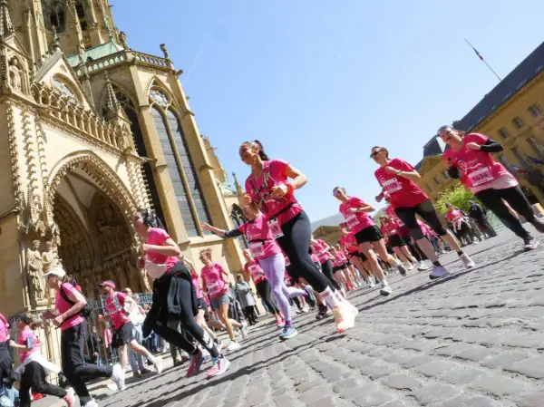 Course de femmes en rose lors du semi-marathon de Tulle, devant une cathédrale majestueuse.