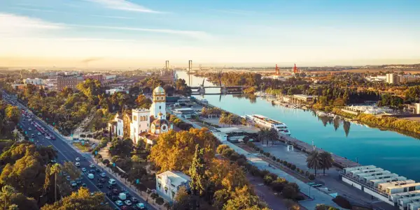 Vue aérienne de Séville au coucher du soleil, avec le Guadalquivir et des bâtiments historiques. Imaginez les coureurs du marathon de Séville 2026 traversant ce paysage.